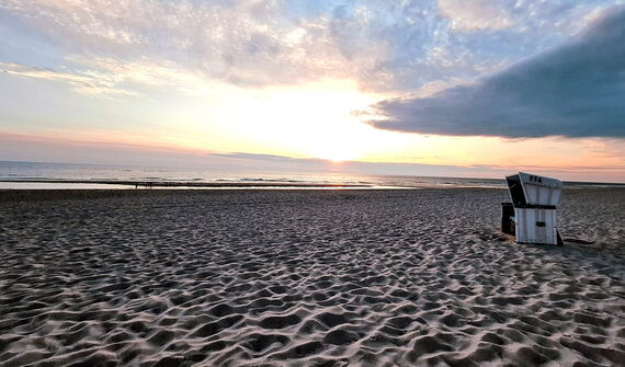 Ein Strandkorb steht vor dem Meer auf einem Sandstrand im Sonnenuntergang